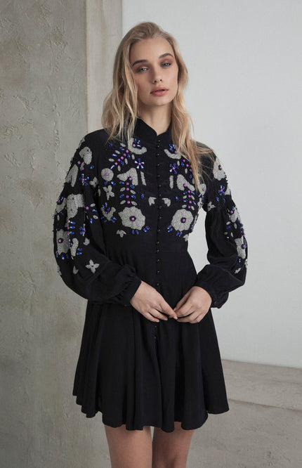 Woman wearing a black mini dress with floral embroidery and long sleeves