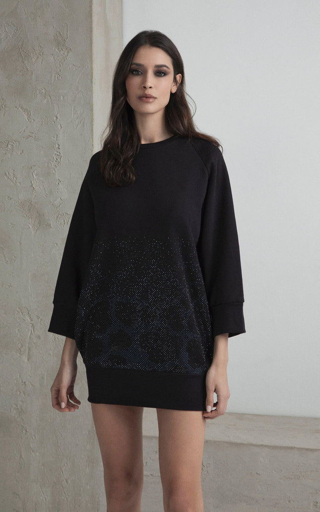 Woman wearing black oversized sweatshirt dress with subtle sparkling details, standing indoors