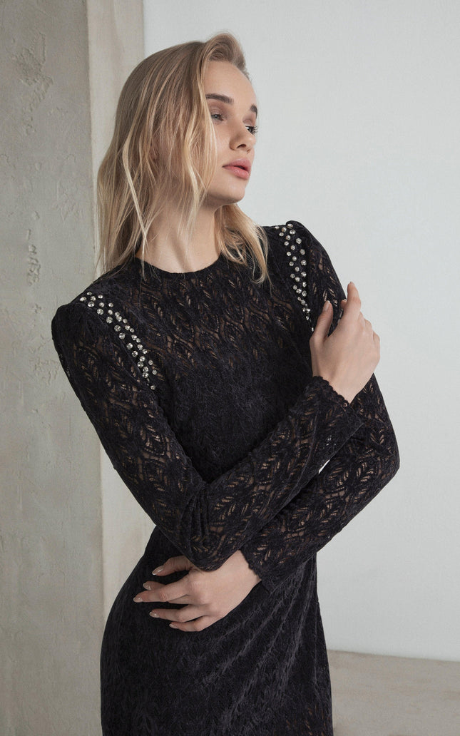 Woman in a black lace dress with studded shoulder details, elegant fashion pose