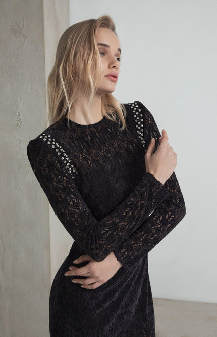 Woman in a black lace dress with studded shoulder details, elegant fashion pose
