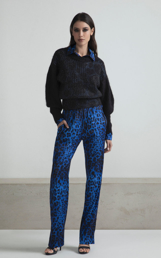 Woman wearing black sweater and blue animal print pants, standing indoors, fashion style