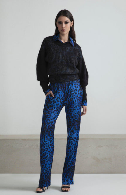 Woman wearing black sweater and blue animal print pants, standing indoors, fashion style