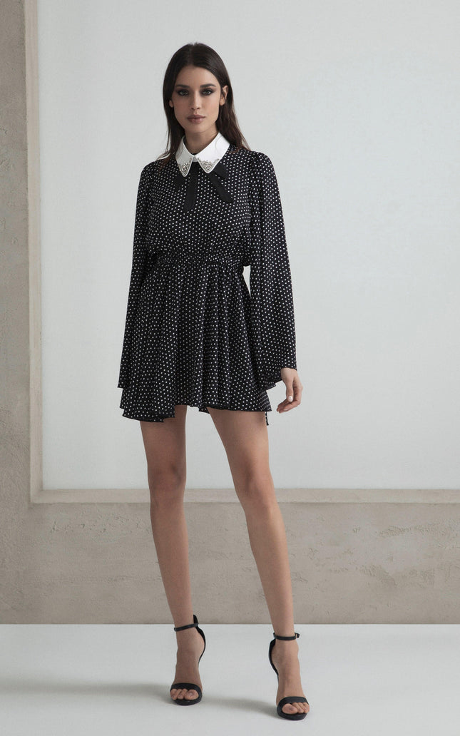 Woman wearing black polka dot mini dress with long sleeves and white collar