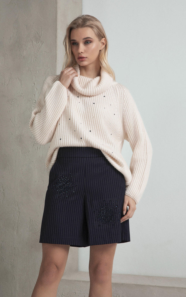 Woman wearing cream knit sweater with bead accents and pinstripe embellished shorts