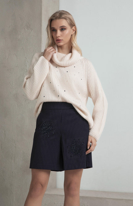 Woman wearing cream knit sweater with bead accents and pinstripe embellished shorts