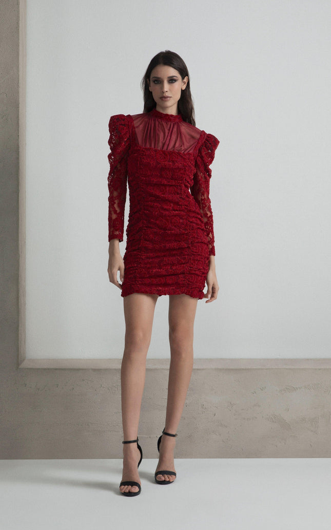 Woman in a red lace mini dress with long sleeves and sheer neckline, wearing black heels