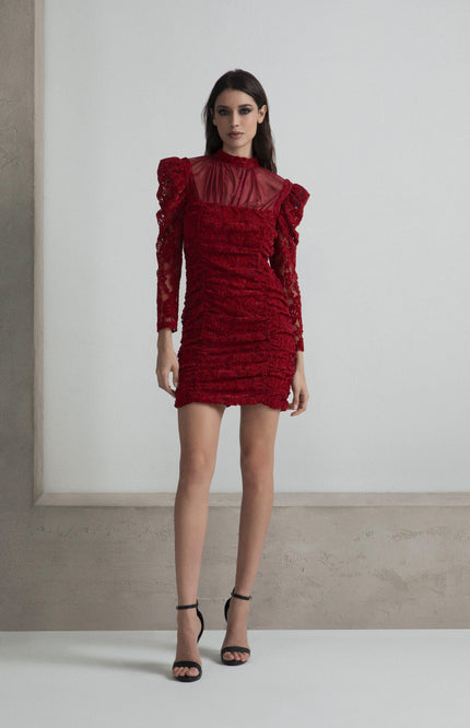 Woman in a red lace mini dress with long sleeves and sheer neckline, wearing black heels