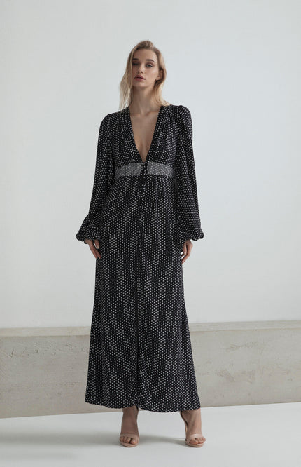 Woman in long black polka dot dress with deep V-neck and beaded waistband