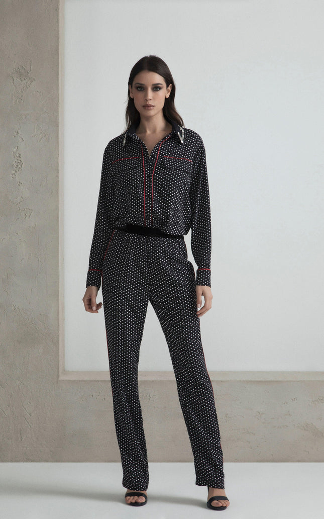 Woman wearing black polka dot blouse and pants set with red trim details, standing indoors
