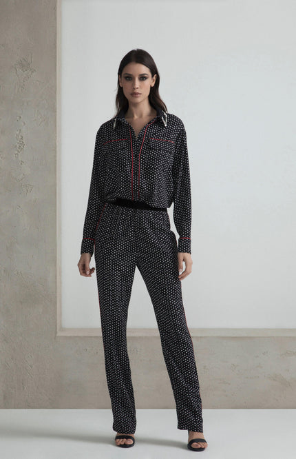 Woman wearing black polka dot blouse and pants set with red trim details, standing indoors