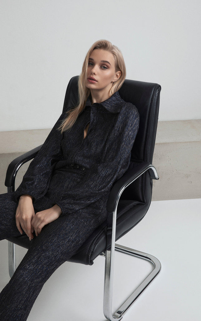 Woman in metallic dark jumpsuit sitting on modern chair, minimalist fashion look