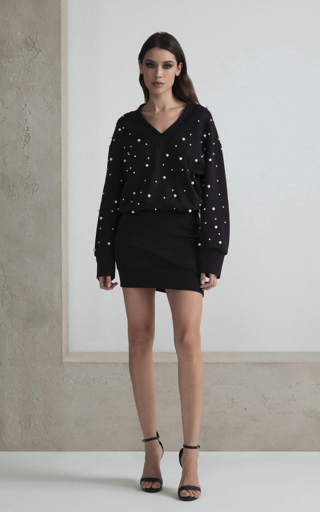 Woman wearing black pearl-embellished sweater and mini skirt set, standing indoors