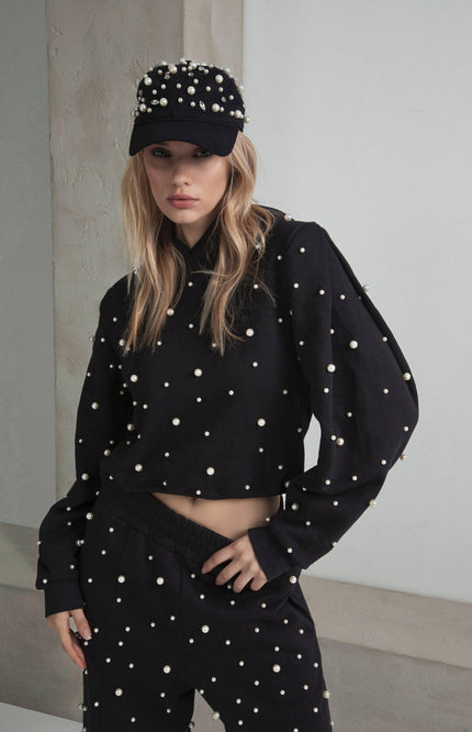 Woman wearing black pearl-studded sweatshirt, pants, and cap, modern fashion look