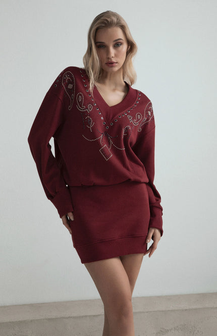 Woman wearing a burgundy embellished V-neck sweater dress with decorative studs