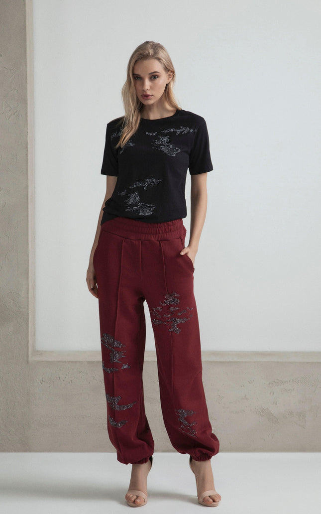 Woman in black embellished t-shirt and red jogger pants with rhinestone details, neutral background
