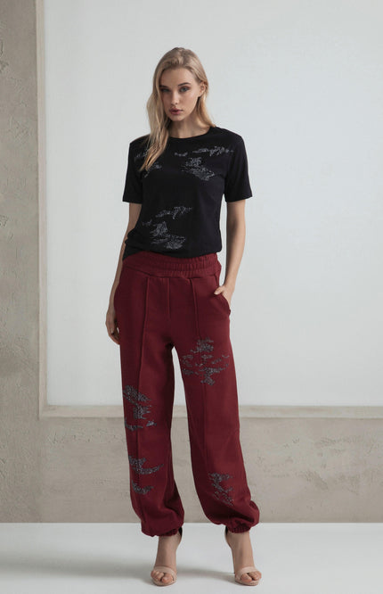Woman in black embellished t-shirt and red jogger pants with rhinestone details, neutral background