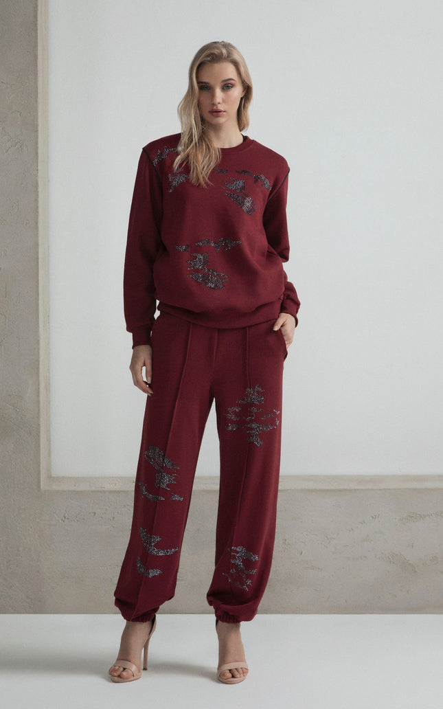 Woman in burgundy embellished sweatshirt and pants set, standing against a light background