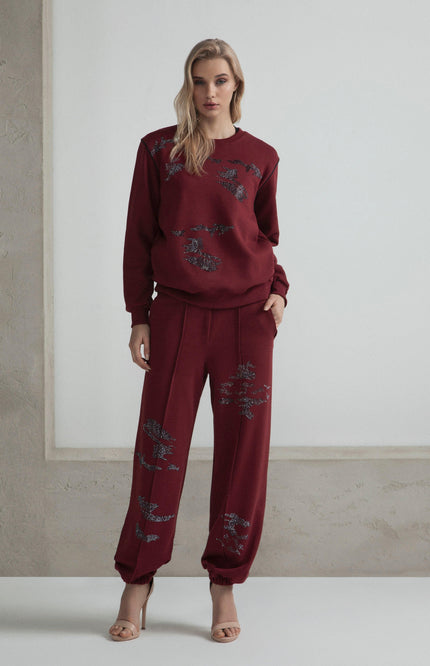 Woman in burgundy embellished sweatshirt and pants set, standing against a light background