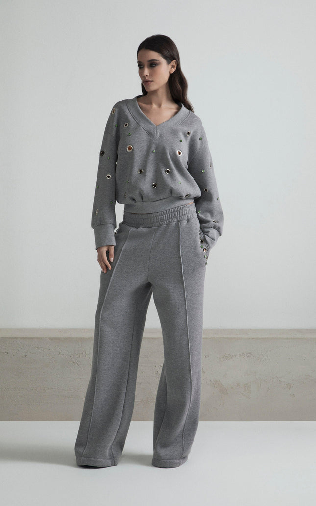 Woman wearing a grey embellished sweatshirt and wide-leg pants in a minimal indoor setting