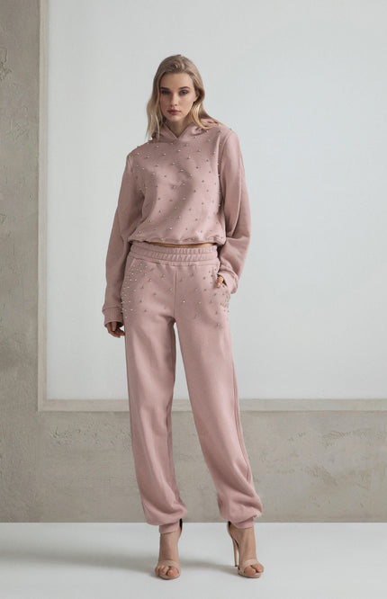 Woman wearing pink embellished sweatshirt and sweatpants set, neutral background