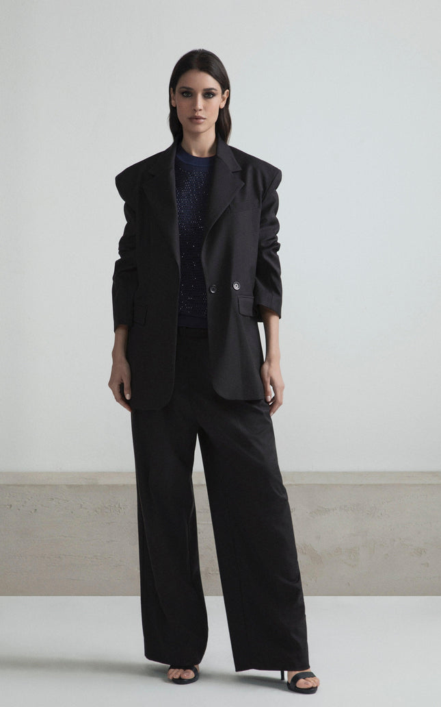 Woman in oversized black blazer, wide-leg pants, and sparkly top, standing indoors
