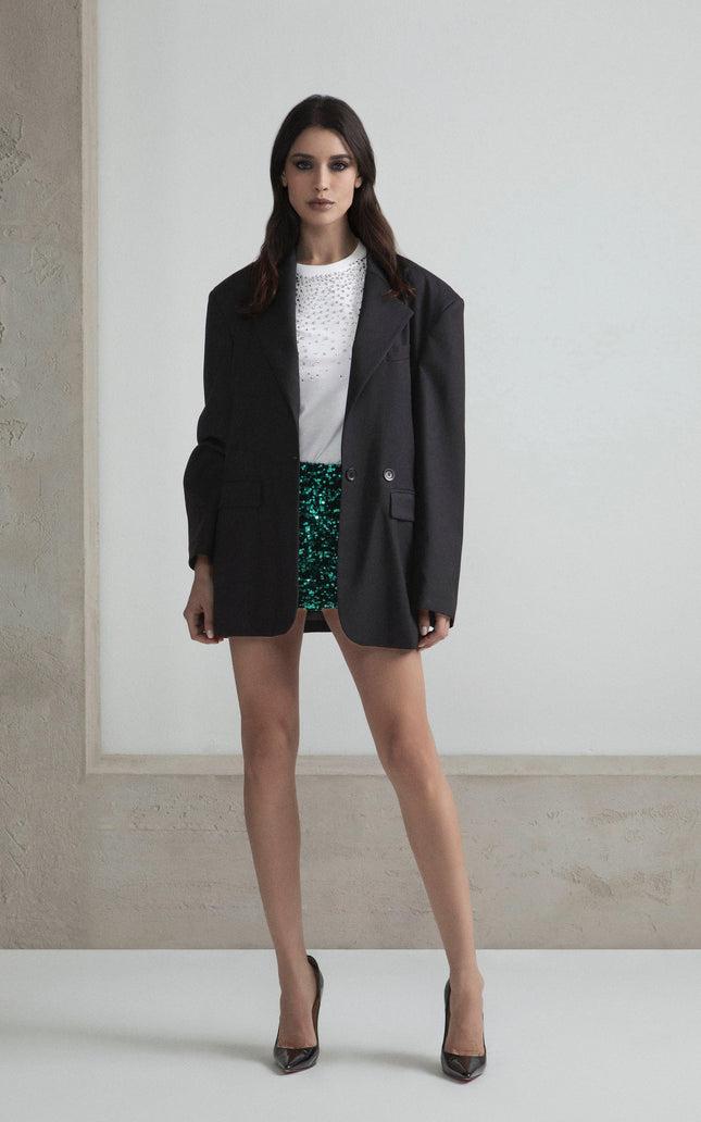 Woman in oversized black blazer, white studded top, green sequin shorts, high heels