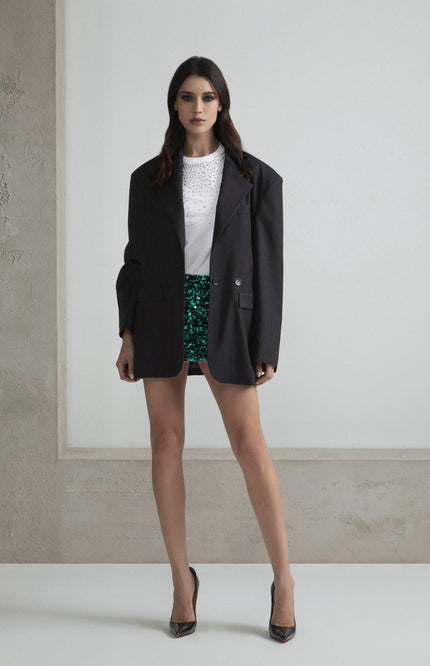 Woman in oversized black blazer, white studded top, green sequin shorts, high heels