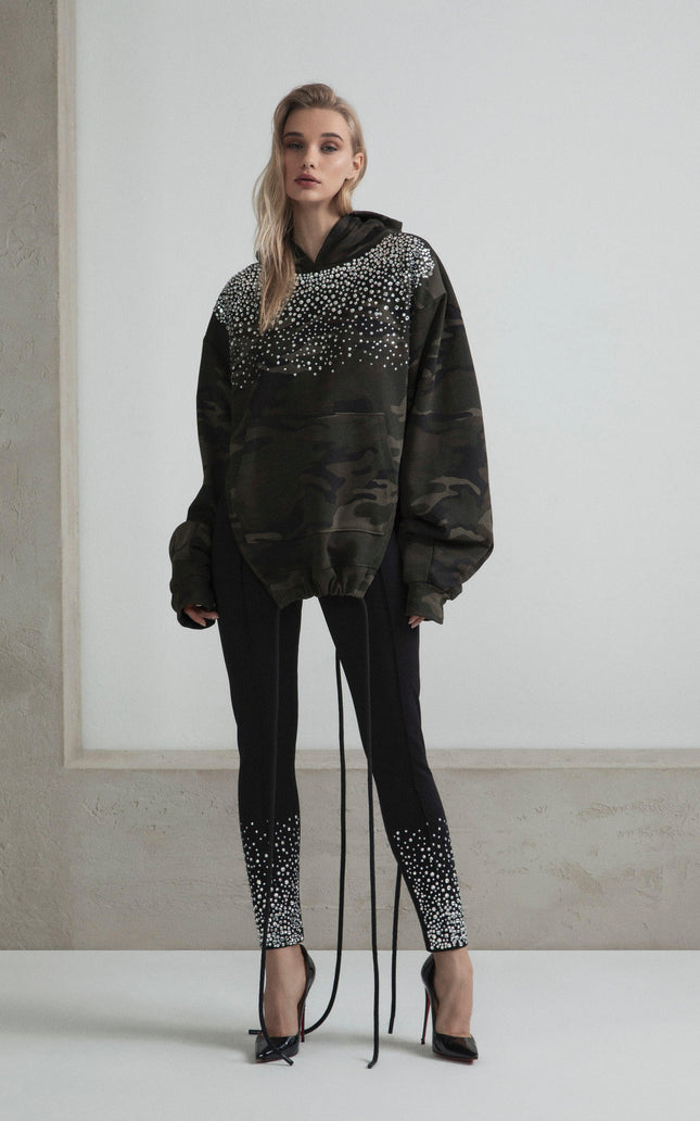 Woman in oversized camo hoodie with crystal embellishments and black pants with crystal details