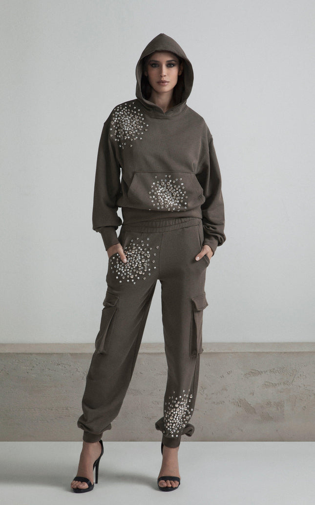 Woman in embellished brown hoodie and cargo pants with rhinestone details, standing indoors