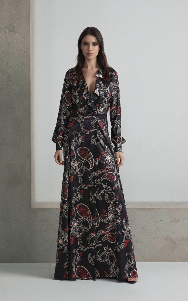 Woman wearing a long black paisley print dress with ruffled neckline in minimalist setting