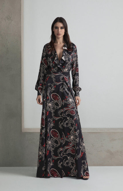 Woman wearing a long black paisley print dress with ruffled neckline in minimalist setting