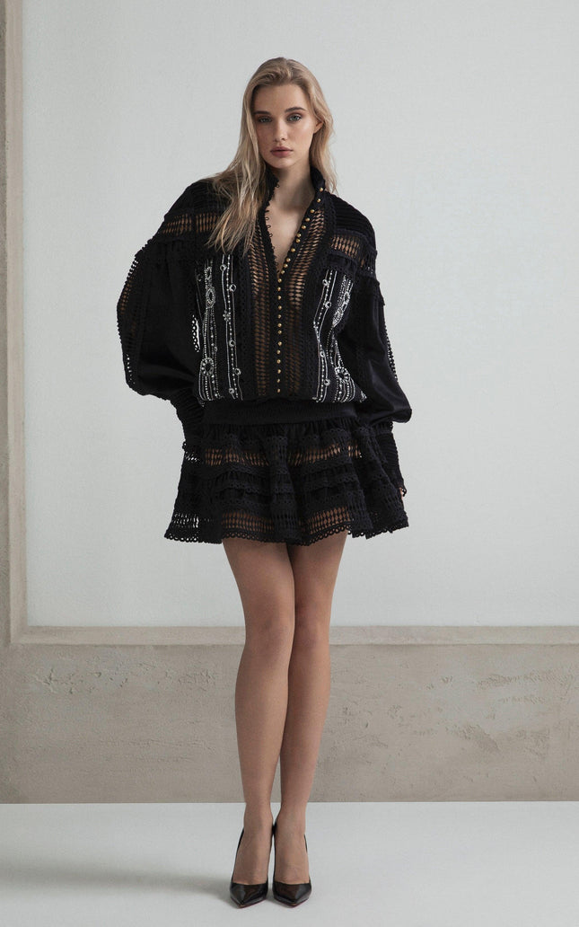 Woman wearing a black embroidered mini dress with sheer details and flared skirt
