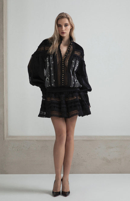 Woman wearing a black embroidered mini dress with sheer details and flared skirt