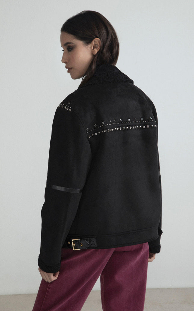 Woman wearing black studded jacket with shearling collar and magenta pants, side view