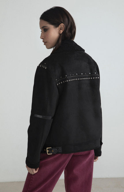 Woman wearing black studded jacket with shearling collar and magenta pants, side view