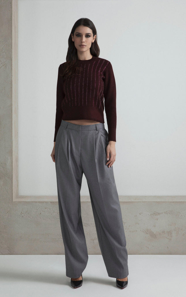 Woman wearing a burgundy sweater and gray wide-leg trousers, standing indoors