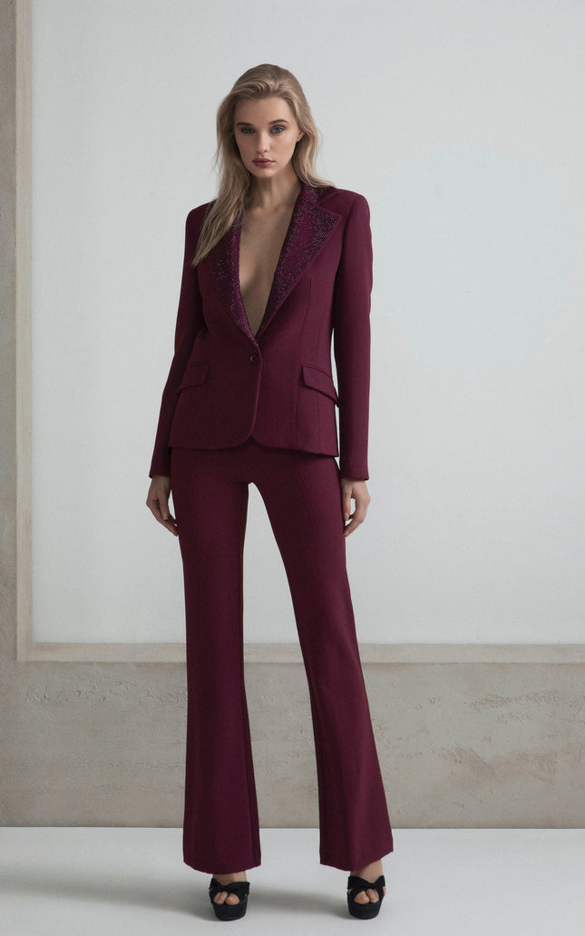 Woman wearing deep burgundy tailored pantsuit with sparkling lapels, standing in minimal setting