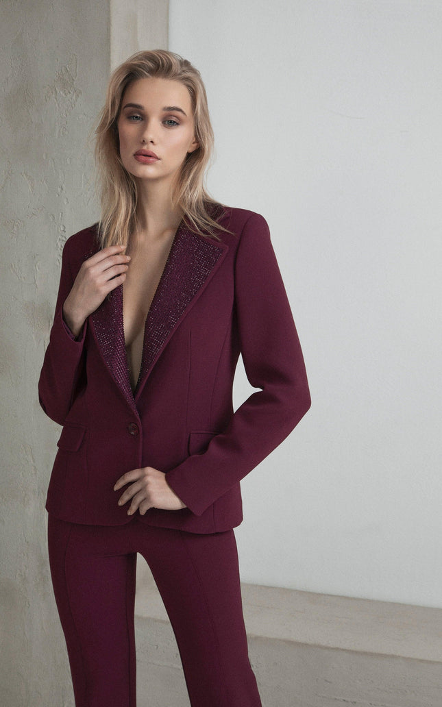 Woman wearing a tailored burgundy pantsuit with embellished lapels standing indoors
