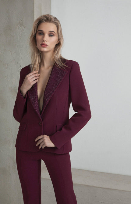 Woman wearing a tailored burgundy pantsuit with embellished lapels standing indoors