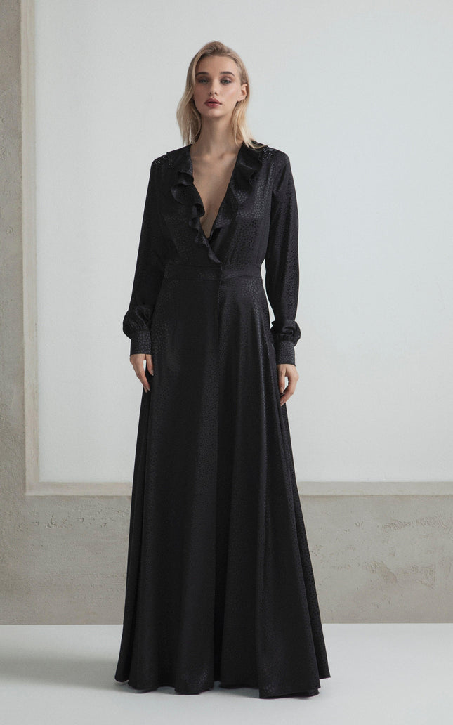 Woman wearing a long black ruffled deep V-neck dress with long sleeves, minimalist background