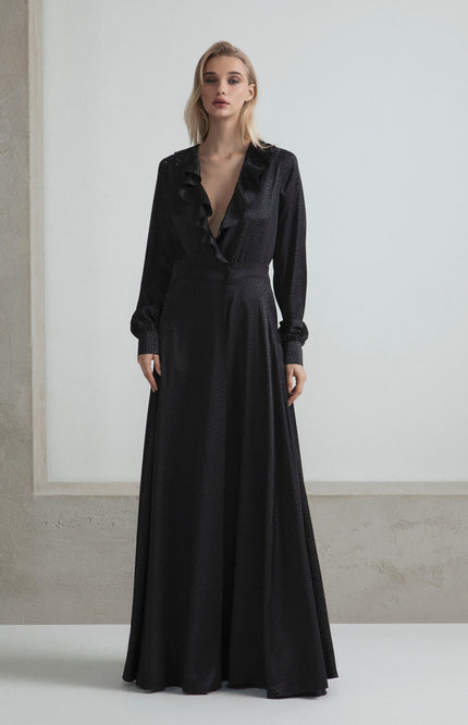 Woman wearing a long black ruffled deep V-neck dress with long sleeves, minimalist background
