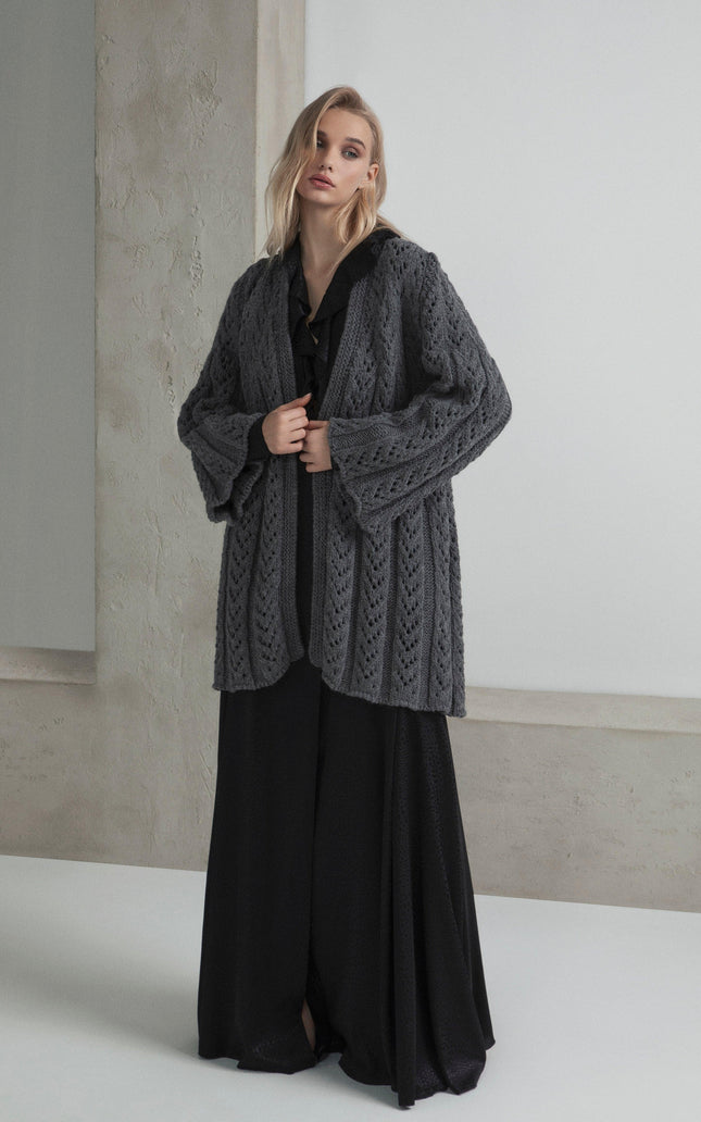 Woman in a chunky grey knit cardigan over a long black dress, minimalist background, fashion look