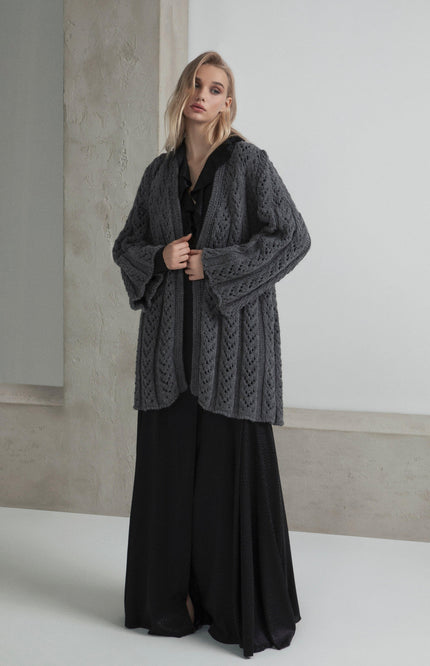 Woman in a chunky grey knit cardigan over a long black dress, minimalist background, fashion look