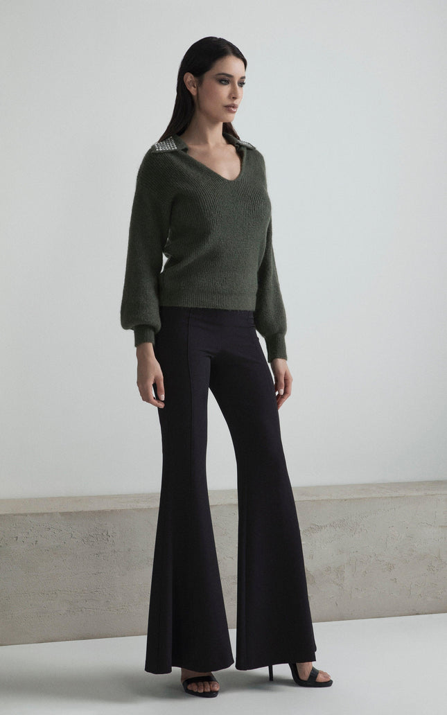 Woman wearing a green knit sweater with embellished collar and black flared pants