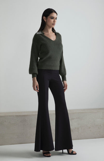Woman wearing a green knit sweater with embellished collar and black flared pants