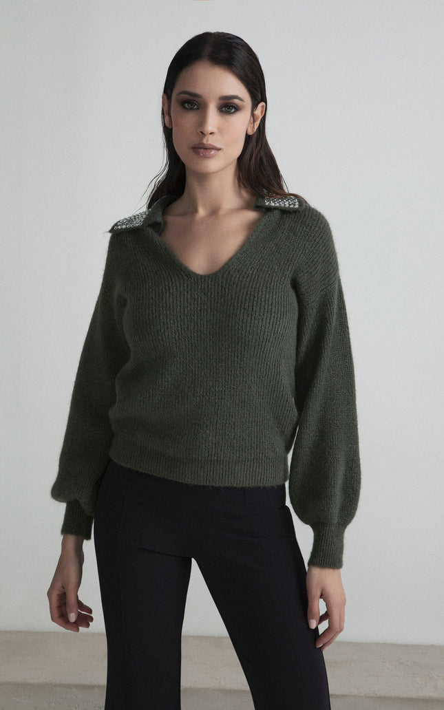 Woman wearing dark green V-neck sweater with jeweled shoulders and black pants