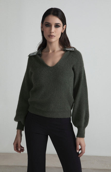 Woman wearing dark green V-neck sweater with jeweled shoulders and black pants