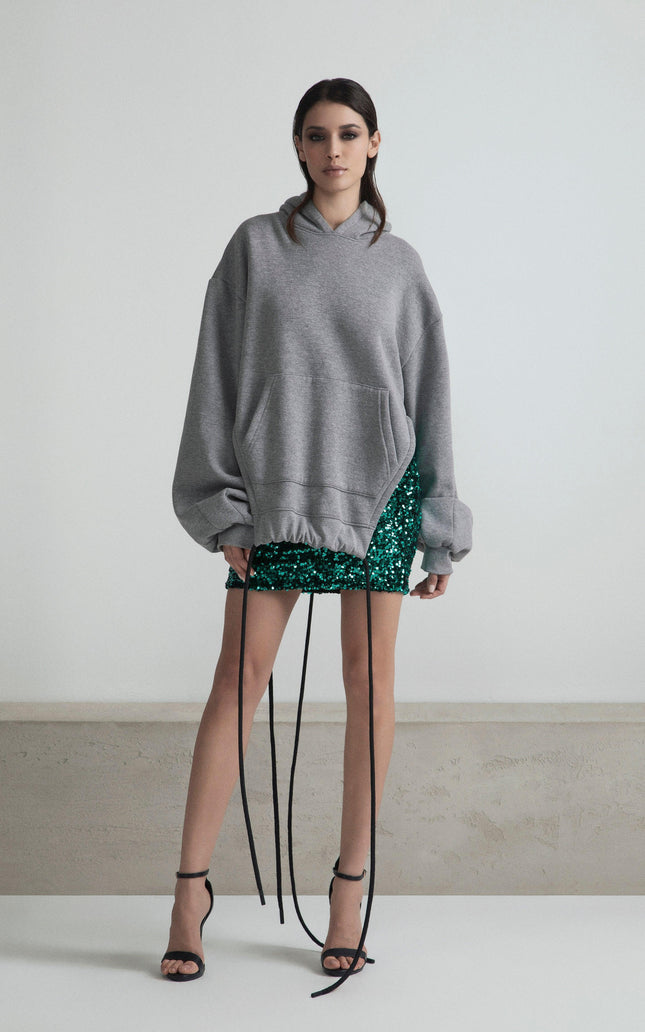 Woman in oversized gray hoodie and green sequin mini skirt with black strappy heels