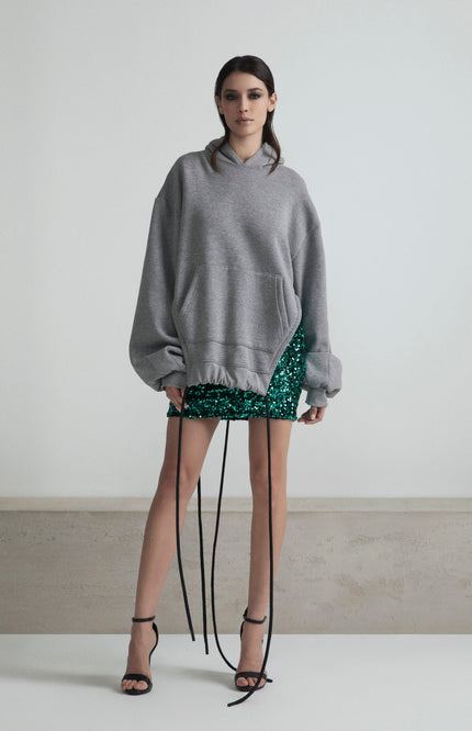 Woman in oversized gray hoodie and green sequin mini skirt with black strappy heels