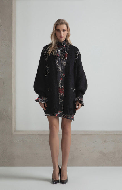 Woman wearing black studded cardigan over a printed mini dress and heels in a minimalist room